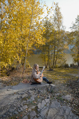 Portrait of smiling caucasian artist plays wooden acoustic guitar in autumnal park. Young songwriter plays string musical instrument hobby outside in nature fall time. Audio music healing in natural