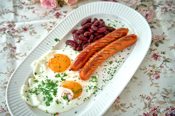 A Delicious Breakfast Platter Featuring Cooked Sausages, Fried Eggs, and Kidney Beans Garnished with Fresh Herbs on a Floral Tablecloth