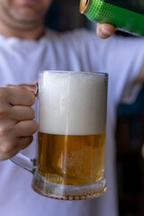 man pouring canned beer into frothy glass mug in front of white t-shirt