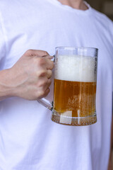 man holding a frothy beer mug in front of white t-shirt