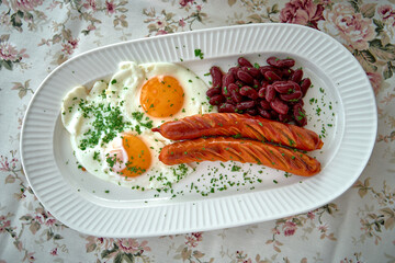 A Delicious Breakfast Plate Featuring Sunny-Side Up Eggs, Tasty Sausages, and Flavorful Red Kidney...