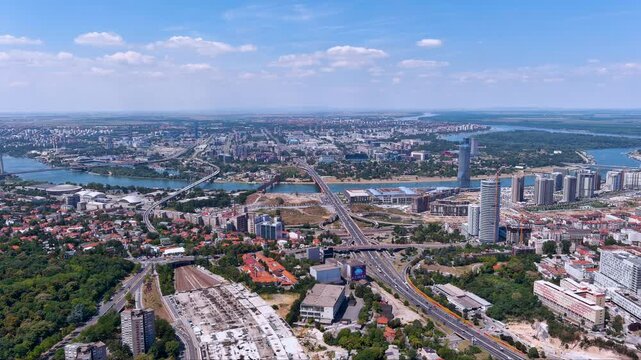 Sweeping drone view of Belgrade, Serbia showing the Sava and Danube rivers, Gazela Bridge, Kula Belgrade and the new Belgrade Waterfront skyline with highways under a bright summer sky.