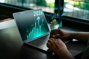 Businessman analyzing digital financial growth charts with upward trends and 2026 target, using laptop and stylus for strategic planning, investment forecasting, future business performance analysis