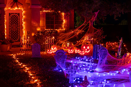 Glowing outdoor decorations with pumpkins, tombstones and orange and purple garlands on the house porch