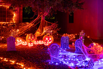 Glowing outdoor decorations with pumpkins, tombstones and orange and purple garlands on the house porch