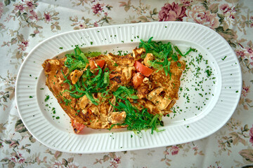 A Deliciously Crafted Omelet Garnished with Fresh Herbs, Tomatoes and Greens Served on a Decorative Plate Perfect for a Hearty Meal.