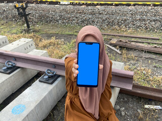 Hijab woman using smart phone with blue screen on railway station