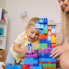 Child and mother building towers with colorful toy blocks at home