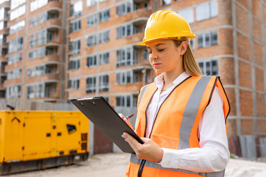 Confident female engineer inspecting construction site with clipboard and hard hat