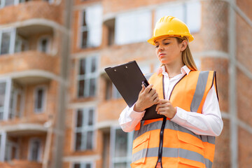 Female construction worker inspecting a site with clipboard and safety gear