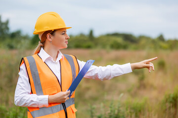 Female construction worker pointing outdoors in safety gear and hard hat