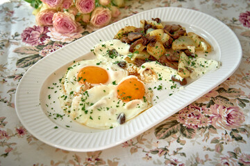 Delicious Breakfast Platter Featuring Two Eggs Sunny-Side Up Topped with Creamy Sauce Served with Seasoned Potatoes and Fresh Herbs Amidst Floral Decor