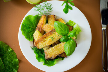Fried zucchini slices with salad greens on a brown background