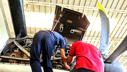 Two mechanics performing maintenance on a turboprop engine inside an aircraft hangar with tools