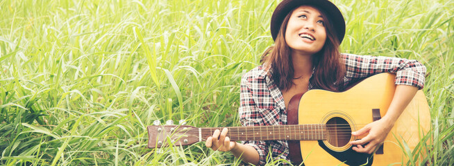 Banner women playing acoustic guitar outdoor in green park. Woman playing acoustic guitar music instrument at home. Wide Asian musician girl lifestyle in green nature. Happy guitarist with copy space