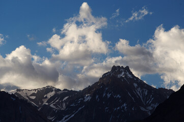 A night view of snowy mountains with clouds at sunset. The clouds and sky turn a magnificent golden color as the sun sets.