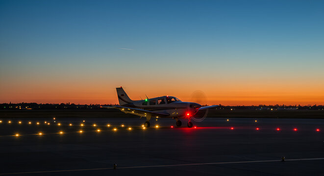 Single-engine aircraft at dusk preparing for takeoff on runway lights ablaze