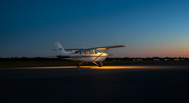 Small airplane illuminated on an airport runway at twilight hour with colorful sky - Powered by Adobe