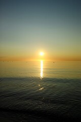 The sun sets over the tranquil ocean, casting a warm glow on the water's surface. The peaceful beach scene reflects the beauty of nature at dusk.