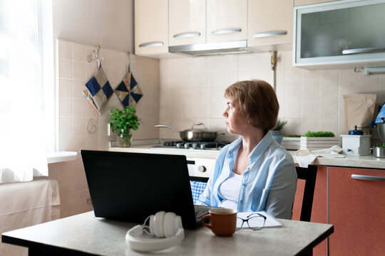 Middle-aged woman working from home office. Workplace in kitchen, laptop. Depressed senior freelancer. Female health problem on retirement, burnout, anxiety. Small slow business, refugee entrepreneur - Powered by Adobe