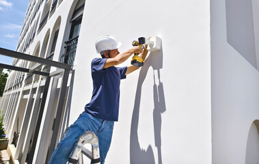 A technician installs a CCTV camera on the facade of a residential building