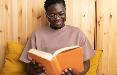Young black man reading a book and smiling at home