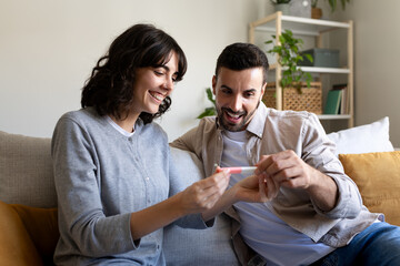 Happy caucasian couple looking at positive pregnancy test together at home.