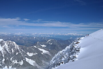 A lone hiker, warmly dressed in winter gear, stands triumphantly at the summit of a snow-covered...