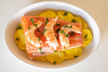 Oven-roasted salmon fillet, seasoned with parsley and accompanied by shrimp and sliced potatoes, creates a nutritious meal rich in omega-3 fatty acids and essential nutrients