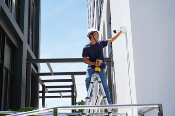A technician installs a CCTV camera on the facade of a residential building