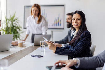 Selective focus on smiling businesswoman with tablet sitting at boardroom with tablet and smiling at camera.