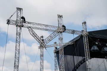 Stage truss system with workers assembling metal scaffolding and lighting rig for outdoor event or...