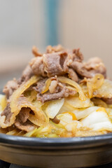 A traditional Asian clay pot rice dish is served piping hot, nestled in a rustic earthenware pot. Steam rises from the sizzling surface, revealing layers of tender sliced meat, crisp bean sprouts