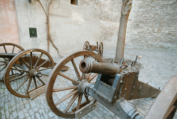 An analog 35mm film photograph captures antique field cannons with wooden wheels in a Prague courtyard, highlighting their rustic texture and historical detail.
