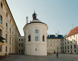 A sunlit analog 35mm film photograph captures the historic Prague Castle courtyard with its distinctive rotunda, devoid of crowds.