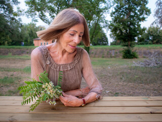 Mature woman tenderly clasping floral arrangement while leaning on rustic wooden surface near Po...