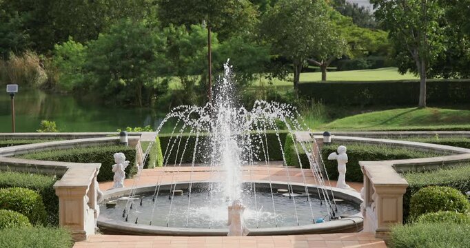 Elegant stone fountain in lush garden with statues, water jets, surrounded by greenery, peaceful atmosphere, ideal for park or landscape design concepts.