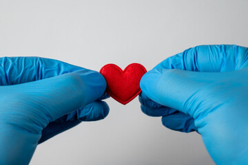 Hands in Medical Gloves Holding a Small Fabric Heart on White Background