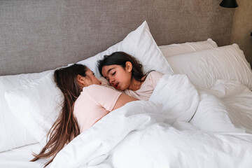 Two girls are sleeping in a bed with white sheets. One of the girls is wearing a pink shirt