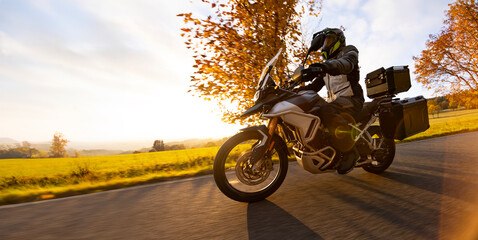 Driver riding motorcycle on empty road during sunset, autumn mountains