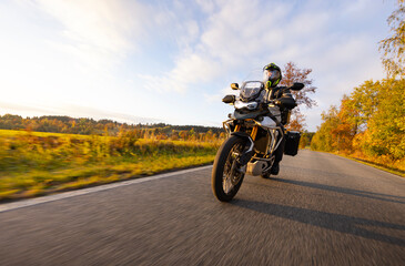 Driver riding motorcycle on empty road during sunset, autumn mountains