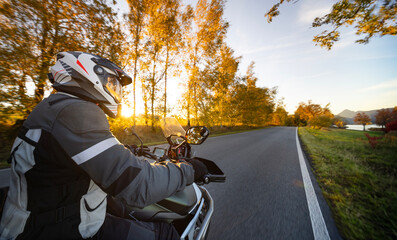 Driver riding motorcycle on empty road during sunset , view from the passenger side