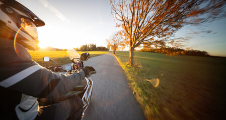 Driver riding motorcycle on empty road during sunset , view from the passenger side