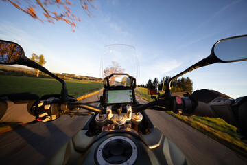 Driver riding motorcycle on empty road during sunset , view from the handlebars