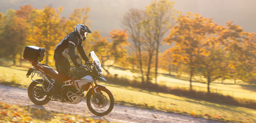 Driver riding motorcycle on empty road during sunset, autumn mountains