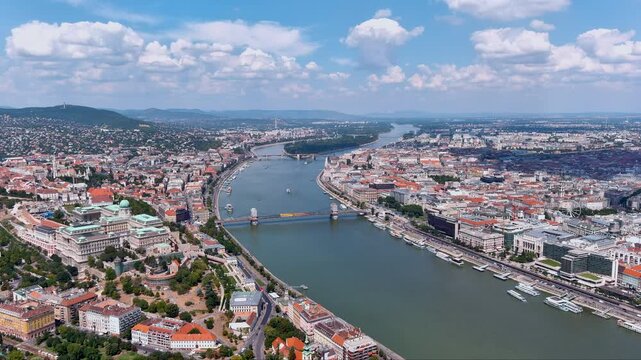 Sweeping drone view over Budapest, Hungary showing the Danube, Szechenyi Chain Bridge, Buda Castle and the Pest waterfront with boats and historic architecture under summer skies.