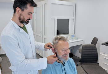 Audiologist expertly adjusts a hearing aid with specialized equipment for better senior man patient fitting. Individual hearing aid fitting