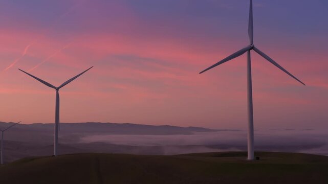 Wind turbines stand tall on rolling hills, generating clean energy at sunrise in Altamont Pass, Livermore, California, USA. The pink sky reflects the promise of a sustainable future.