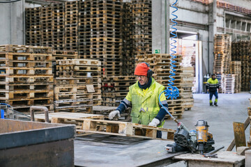 Carpenter wearing safety gear actively working on a wooden pallet inside a recycling factory, contributing to sustainable practices in manufacturing