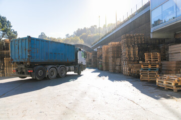 Truck is leaving a wooden pallet recycling industry area with stacked pallets and wooden planks...